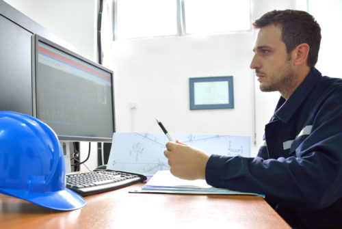 Man sitting at a desk, holding a pen, and looking at a desktop computer